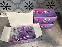 Three boxes of FrozCup reusable coffee and tea filters in purple, unopened except one box opened to show six filters inside wrapped individually in plastic.