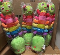 Four colorful plush caterpillar toys displayed in original plastic packaging, showing rainbow-striped bodies and green heads with smiling faces.