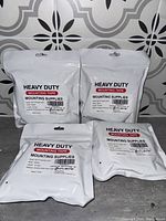 Four packs of Heavy Duty Mounting Tape in sealed white packaging with clear printed labels showing brand and description.