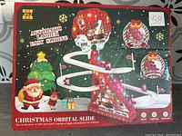 Box front view showing the Christmas Orbital Slide decoration with Santa and reindeer sliding on a curved track around a red Christmas house base with music and lighting features.