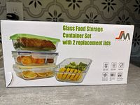 Box front showing glass containers stacked with food inside, highlighting 2 replacement lids included and multi-use safe features.