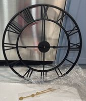 Front view of black metal wall clock frame showing large Roman numerals and black clock hands installed