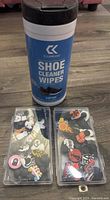 Container of CleanKicks shoe cleaner wipes along with two plastic containers of assorted Crocs shoe charms featuring cats and basketball motifs.