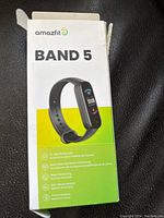 Open box showing Amazfit Band 5 packaging with product image and features listed: 15 day battery life, heart rate, oxygen, stress monitor, sleep monitor, voice assistant.