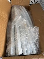 Open box showing white metal garden arch parts wrapped in clear plastic, including straight tubes and fittings.
