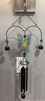 Full front view of metal butterfly wind chime hanging on a wall, showing details of hanging bells and chimes.