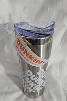 Front view of stainless steel Dunkin Donuts tumbler with clear lid, straw, and attached label.