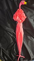 Folded pink flamingo umbrella showing ruffled fabric and flamingo head handle.