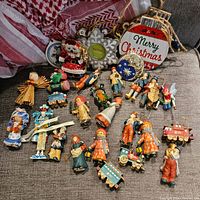 Photo showing a variety of hand-painted wooden figurine Christmas ornaments, including children and angels, miniature trains, and some larger round ornaments with Merry Christmas text.