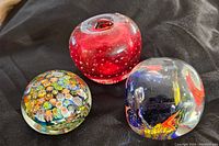 Three vintage glass paperweights: red swirl with bubbles, millefiori floral dome, clear glass sphere with colorful internals