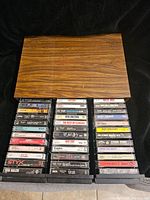 Wooden case with numerous cassette tapes arranged in 4 columns beneath it showing a variety of vintage rock albums.