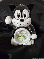 Front view of the black and white cat-shaped ceramic alarm clock showing the clock face and the cat figurine detail.