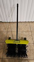 Full view of the RYOBI Expand-It rubber sweeper attachment showing dual cylindrical rubber brush rollers, wheels, and connection pole.