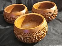 Three vintage wooden bowls with carved floral and geometric designs, side view showing the detailed carving and wood grain with minor wear.