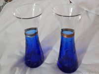 Two blue and clear glass bud vases shown side by side on white background