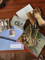 Contents of the box spread on a wooden surface showing the pencil, blue writing pad, envelopes, lavender sachet, gift cards, and blank book featuring art prints.
