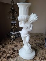 Front side view of the white ceramic cherub statue holding the urn vase, showing detailed sculpting on the cherub and vertical fluted design on the vase.