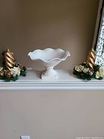 White vintage ceramic pedestal compote displayed on a white mantel flanked by gold and floral decorations.
