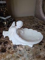 Side angle showing the cherub figurine leaning on the edge of the shell-shaped candy dish, highlighting the detailed facial features and wing design