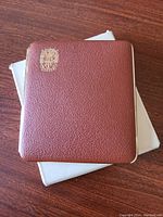 Brown leather cigarette case with gold tone Austin crest on front.