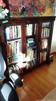 Full view of dark wooden display cabinet with three glass doors filled with books