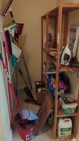 Full view of cleaning items arranged in corner with shelf rack, mop bucket, and cleaning tools leaning on the wall.