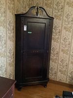 Full view of antique dark wood corner cabinet with single door and decorative top finial.