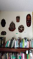 Wall display showing six masks above bookshelf