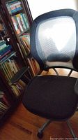 Front view of black office chair with mesh backrest and fabric seat next to bookshelf.