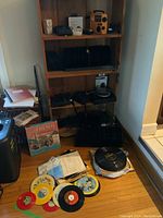 Records on the floor with 45 RPM and 78 RPM vinyl, some records in sleeves, vintage audio materials and boxes.