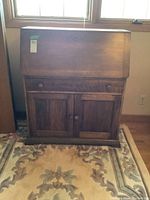 Front view of the closed solid wood secretary desk showing the drop-front surface and two lower cabinet doors.