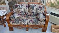 Front view of rattan sofa with floral cushions showing two seats and armrests.