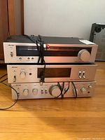 Front view of three stacked Aurex stereo components including tuner, power amplifier, and preamplifier on a wood floor.