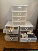 Three plastic storage drawers stacked; two drawers open showing cassette tapes inside.