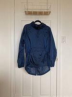 Full view of navy blue DKNY raincoat hanging on a black hanger against a white door.