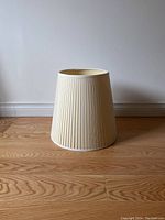 Full view of cream colored pleated fabric lampshade on wood floor, shown upright