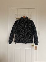 Front view of black and grey leopard print puffer jacket hanging on door, showing full zipper, high collar and elastic cuffs.