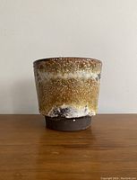Front view of the cylindrical mid-century modern ceramic planter showing the mottled brown, beige, and white textured glaze with natural dripped glaze effect near the base.