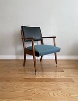 Front view of mid-century modern walnut armchair with black leather backrest and blue fabric seat, showing wooden armrests and metal-tipped tapered legs.