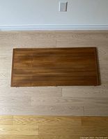 Top view of rectangular teak dining table leaf, showing wood grain and frame edges.