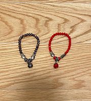 Two bracelets laid flat; one with dark purple faceted stone beads and metal charms, the other with bright red stone beads and metal charms.