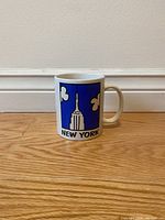 Front view of vintage Mary Ellis New York mug featuring Empire State Building graphic on blue background