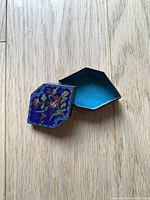 Enamel trinket box opened to show partitioned interior with turquoise enamel finish.