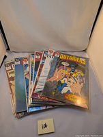 Photo shows a stacked group of 12 comic books from The Outsiders series laid out on surface.