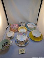 Nine assorted vintage teacups and saucers with various floral patterns and gold trim arranged in a group photo