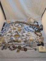 Overview of assorted costume jewelry spread on cloth background including necklaces, brooches, earrings, and pins