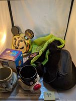 Photo of signed Goofy glove/hat, Winnie the Pooh piggy bank in box, and two ceramic cups featuring Bugs Bunny and Sylvester characters.