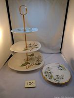 3 tier cake plate with dogwood design on three square plates, gold metal rod and handle. Two separate round Royal Albert side plates with floral dogwood design and gold scalloped edges.