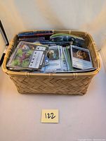 Wide shot of a woven basket filled with a large quantity of trading cards, some sleeved, mostly Chaotic TCG cards.