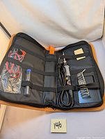 Soldering tool kit in open zippered case showing soldering iron, wire spool holder, small blue container with wires, and other components.